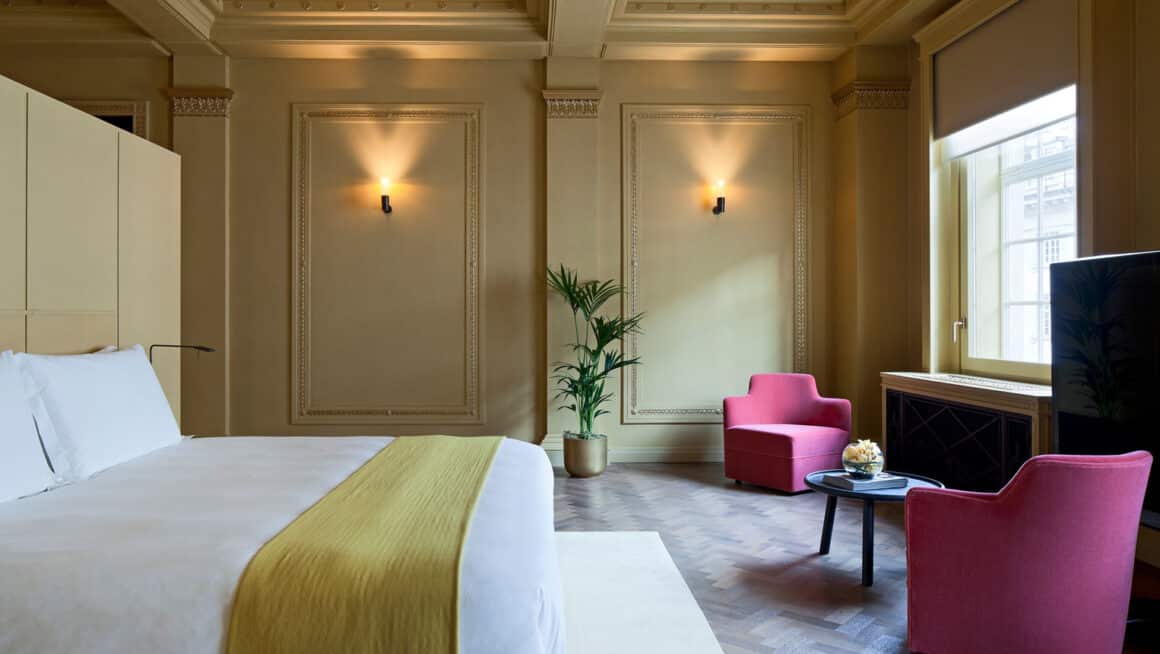 Luxurious suite at Cafe Royal featuring a king-sized bed, cozy pink seating area, warm ambient lighting, and classic décor, offering an elegant stay with Natlaupa.