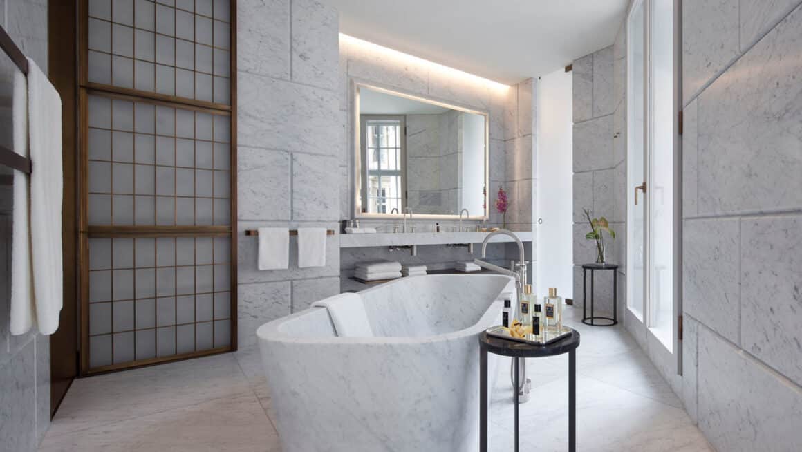 Luxurious bathroom in Cafe Royal Regent Suite 3 with a freestanding marble bathtub, elegant vanity area, and soothing lighting, offering a serene experience with Natlaupa.