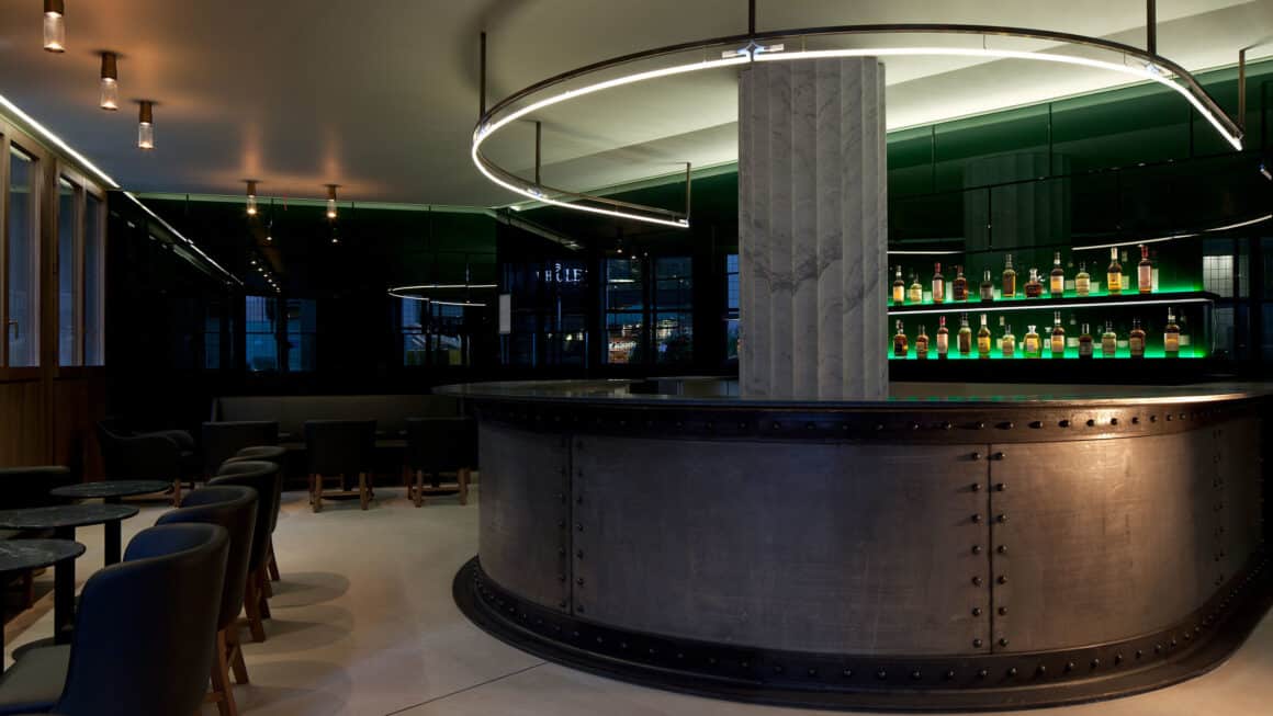 Modern industrial-style bar at Cafe Royal with sleek metal and marble design, cozy seating area, and sophisticated lighting, offering a refined experience with Natlaupa.