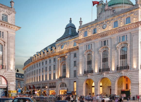 Stunning exterior of Hotel Cafe Royal London, showcasing neoclassical architecture, grand arches, and ambient evening lighting, offering a deluxe experience with Natlaupa.