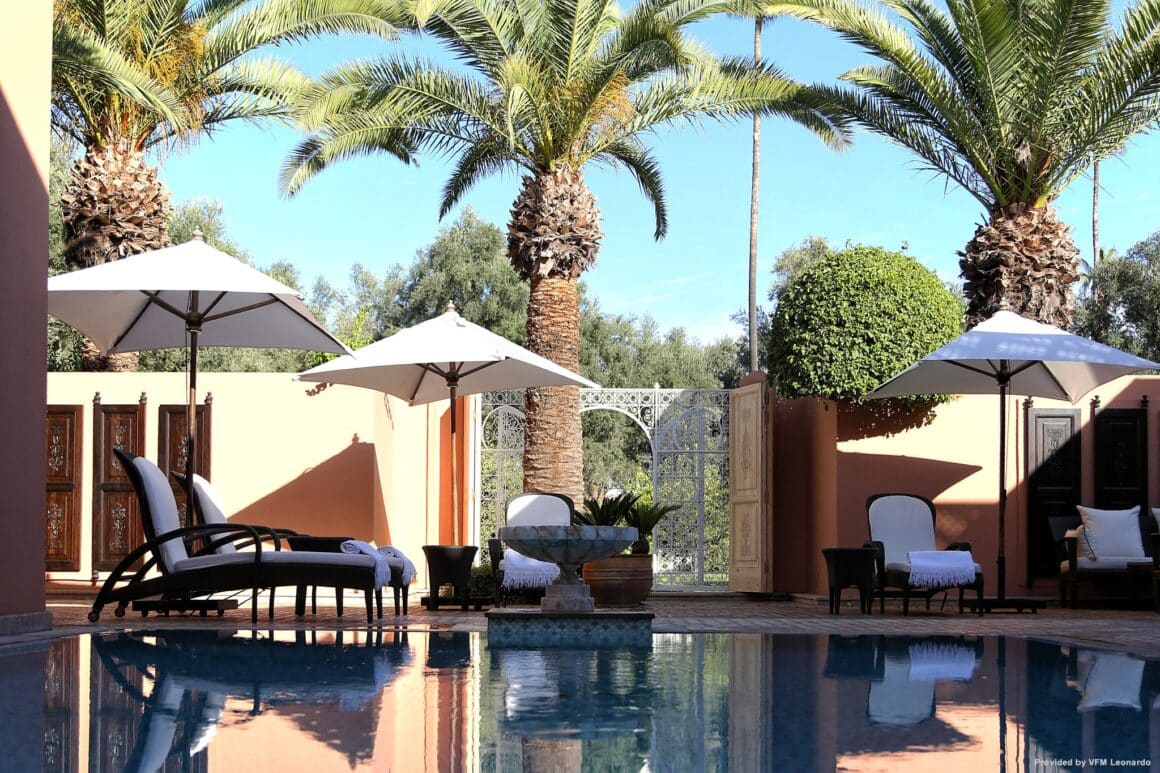 Luxurious outdoor seating area of La Mamounia Marrakesch Suite, featuring plush lounge chairs, palm trees, and a serene private pool with Natlaupa.