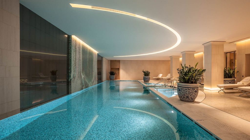 Luxurious indoor swimming pool with modern design, curved ceiling lighting, elegant lounge chairs, and stylish planters, available with Natlaupa.