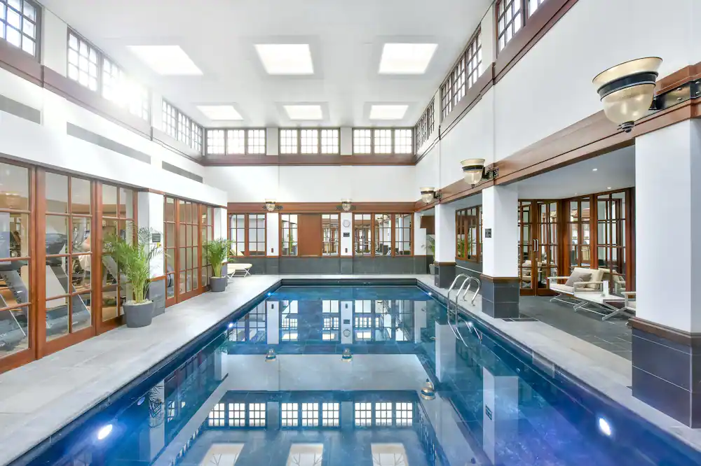 Luxurious indoor swimming pool with elegant wooden accents, natural light, and comfortable seating area, offering a serene retreat with Natlaupa.