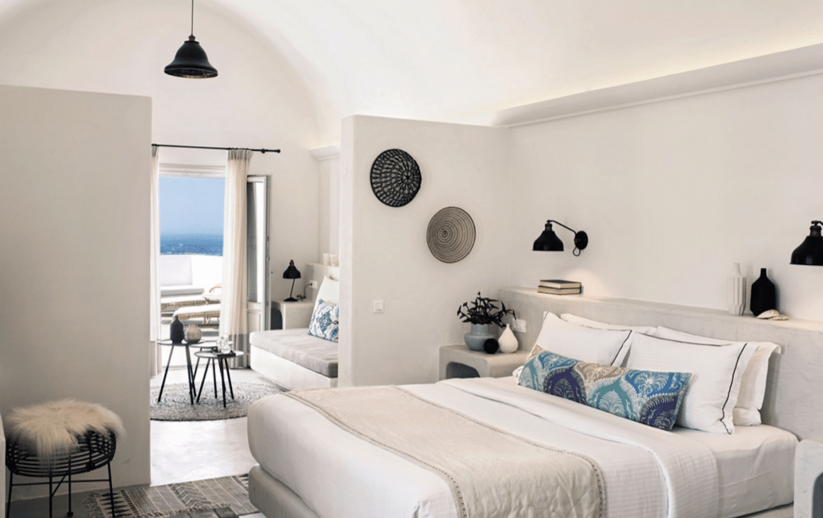 Experience serene luxury in a beautifully designed room at Santo Maris Oia with Natlaupa, featuring ocean views and elegant décor.